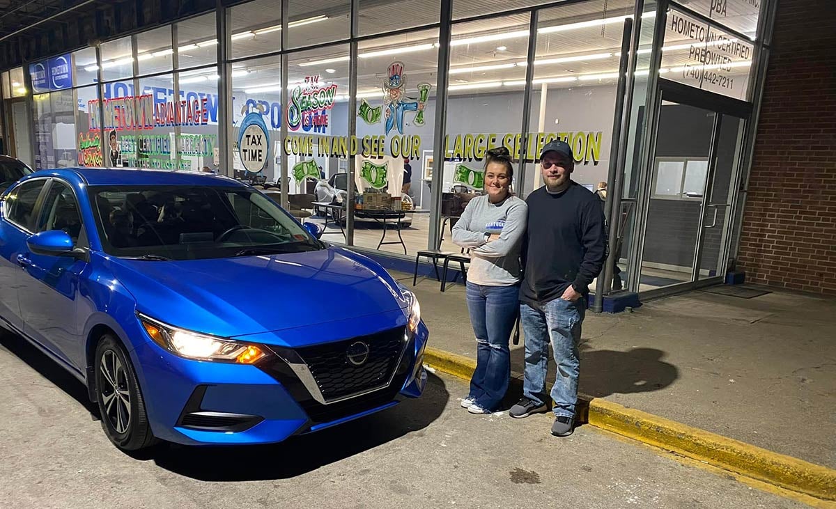 A happy couple next to their newly-purchased used blue Nissan sedan at out Ironton, OH dealership